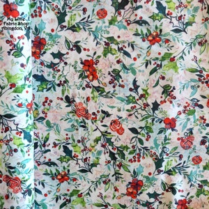 May include: A roll of fabric with a festive floral pattern. The design features red roses, berries, and green holly leaves on a white background. The fabric has a watercolor-like effect, with the text "My Little Fabric Shop Abingdon, Va" visible.