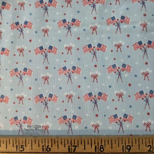 May include: Light blue fabric with a repeating pattern of American flags, red bows, and stars. The flags are red, white, and blue. The text "My Little Fabric Shop Abingdon, VA" is visible.