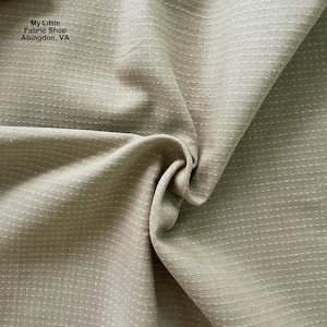 May include: A close-up shot of a folded fabric in a muted green-grey hue. The material features a textured surface with small, evenly spaced white dots. The text "My Little Fabric Shop Abingdon, VA" is visible.