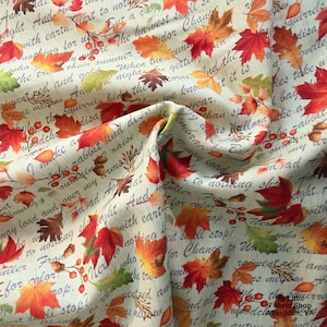 May include: Cream-coloured fabric with a seasonal autumn pattern. The design includes red, orange, and green leaves, acorns, and berries. The fabric also features handwritten text scattered across the surface.