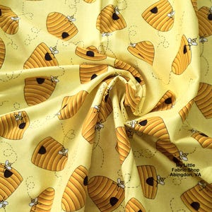 May include: Yellow fabric with a repeating pattern of brown beehives and bees. The beehives have a textured appearance with a dark opening. Bees are depicted flying around the beehives with dotted flight paths. The fabric is folded, creating shadows and depth.