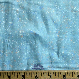 May include: Light blue fabric with a speckled pattern in white, orange, and blue. The fabric has a textured appearance and is suitable for various crafting projects. The text "My Little Fabric Shop Abingdon, VA" is visible.