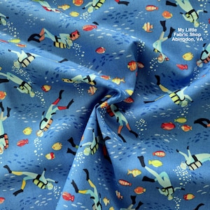 Op de afbeelding: Blauwe stof met een herhaald patroon van duikers en kleurrijke vissen. De duikers hebben rode, gele en zwarte accenten. De stof bevat ook de tekst "My Little Fabric Shop Abingdon, VA".