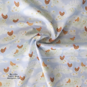 Puede incluir: Tela azul claro con un patrón repetido de gallinas marrones, vallas blancas y hierba verde. Las gallinas tienen crestas rojas y están dispersas por la tela. La tela tiene un aspecto suave y fluido.