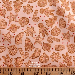 Puede incluir: Tela con un patrón repetido de galletas de jengibre en varias formas, incluyendo estrellas, árboles y hombres de jengibre. Las galletas son de color marrón claro con acentos blancos y rojos, sobre un fondo rosa claro. La tela tiene un tema festivo.