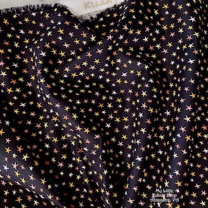 May include: Black fabric with a repeating pattern of small white, yellow, orange, and pink stars. The fabric is folded in half and the text "My Little Fabric Shop Abingdon, VA" is visible in the bottom right corner.