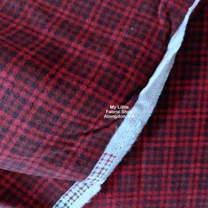 May include: Red and black plaid flannel fabric with a white edge. The fabric is soft and fuzzy. The text "My Little Fabric Shop Abingdon VA" is printed on the fabric.
