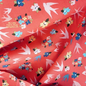 以下が含まれることがあります： コーラル色の生地に、白いツバメと花の模様が描かれています。生地には、白いツバメと、青、黄、白の小さな花束が繰り返し描かれています。画像の左上隅には、「My Little Fabric Shop Abingdon, VA」というテキストが表示されています。