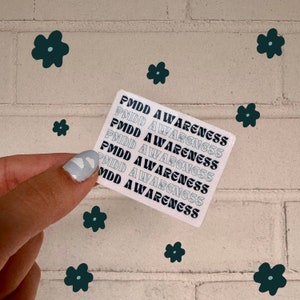 May include: A square sticker featuring the text PMDD AWARENESS repeated in alternating rows of solid black and outlined light blue lettering. The sticker is white with a repeating pattern of the phrase stacked vertically across the entire surface.