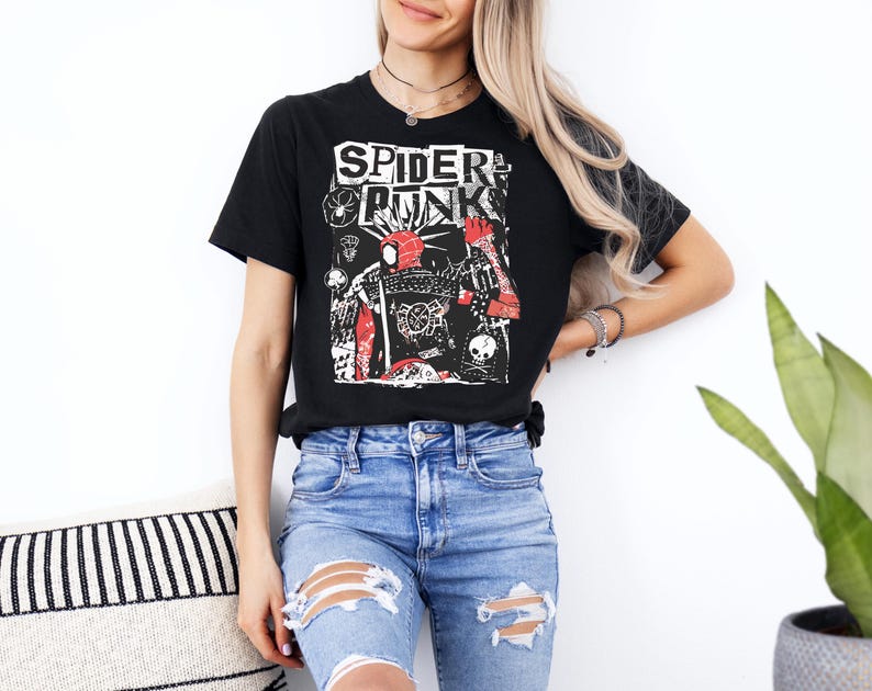 May include: Black t-shirt with the text "SPIDER PUNK" in white, featuring a red and black graphic design. The graphic includes a spider-like figure and other punk-inspired elements. The shirt is paired with blue jeans.