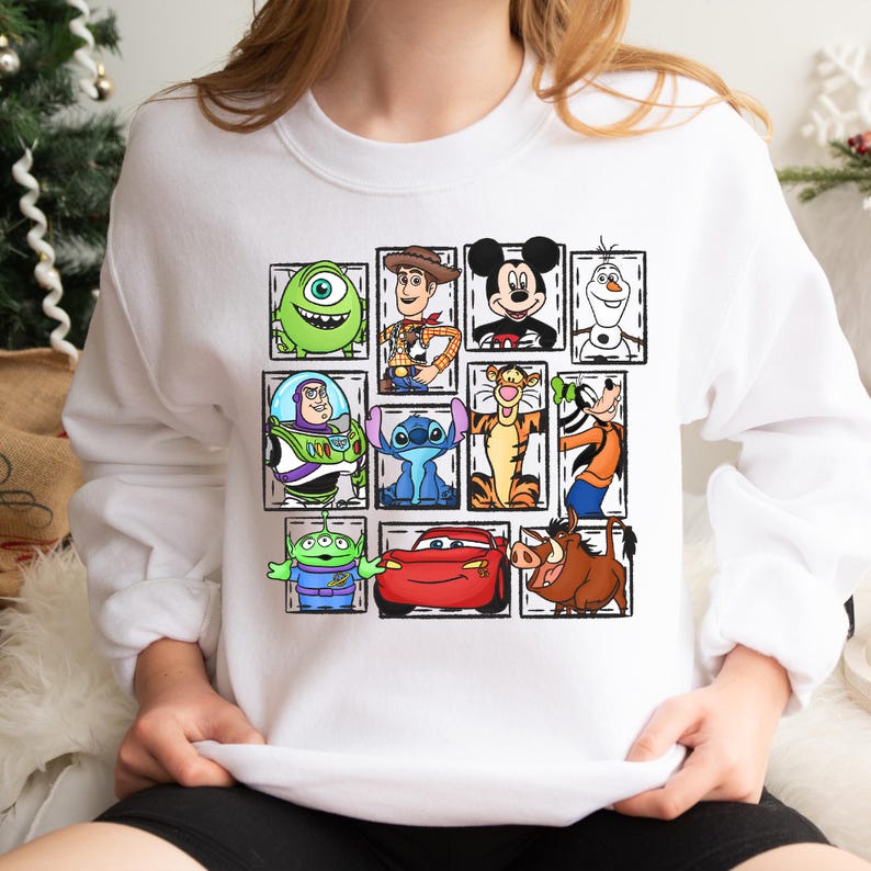 May include: White sweatshirt featuring a collage of cartoon characters including Mike Wazowski, Woody, Mickey Mouse, Olaf, Buzz Lightyear, Stitch, Tigger, Goofy, an alien, Lightning McQueen, and Pumbaa. The characters are in individual rectangular frames.