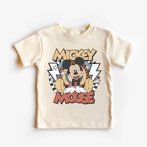 May include: A cream-colored t-shirt featuring a graphic of Mickey Mouse. The design includes the words "Mickey Mouse" in a retro font, with lightning bolts and a checkered background. The shirt is short-sleeved.