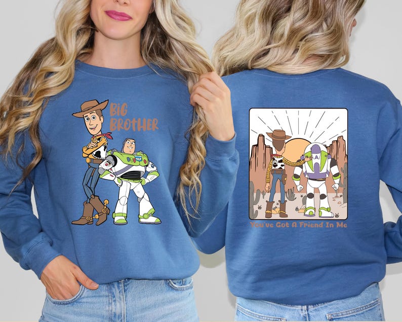Op de afbeelding: Een blauwe sweatshirt met de tekenfilmfiguren Woody en Buzz Lightyear. De voorkant van de sweatshirt heeft de woorden "Big Brother" boven de karakters. De achterkant van de sweatshirt heeft een woestijnsc&egrave;ne met de woorden "You've Got A Friend In Me".