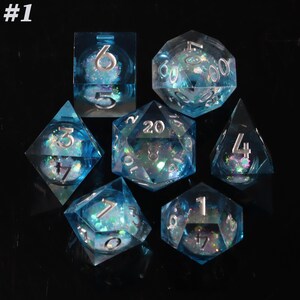 Pode incluir: Conjunto de sete dados poliédricos azuis transparentes com glitter iridescente e numeração prateada. A imagem inclui um quadrado, um d4, um d6, um d8, um d10, um d12 e um d20.
