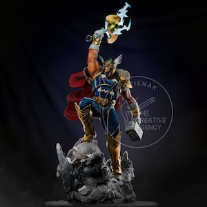 Op de afbeelding: Gedetailleerd beeldje van een superheld in een dynamische pose, met een hamer omhoog. Het figuur is gekleed in een blauw en goud kostuum met een rode cape, staand op een rotsachtige basis. De hamer heeft een gouden kop met blauwe bliksemaccenten.