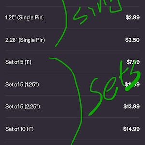 May include: A screenshot of a mobile device displaying a product size chart for single pins and sets of pins. The chart lists sizes from 1" to 2.25" in diameter. The text "MORE BANDO" is at the top.