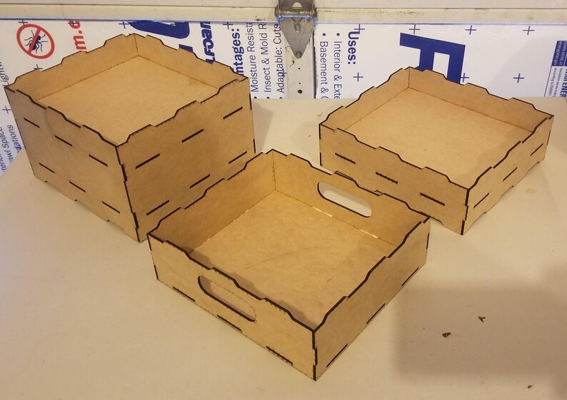 May include: Three wooden boxes with black trim and a cutout handle on the largest box. The boxes are made of a light brown wood and are stacked on top of each other.