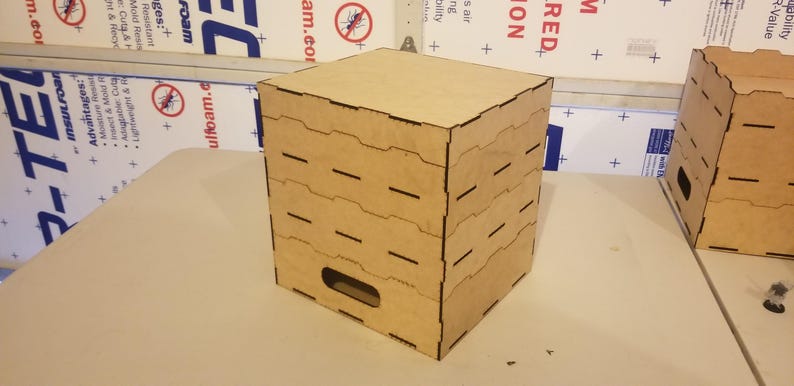 May include: A stackable wooden storage box with a cutout handle. The box is made of light brown wood with black cutouts. The box is empty.