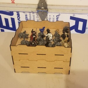 May include: Two-tiered wooden storage box with a brown finish. The box is filled with miniature figures painted in various colors, including blue, red, and gray.