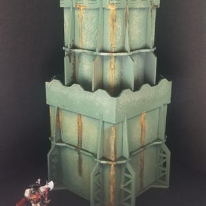May include: A two-tiered, green and brown, cardboard model of a tower with a textured surface. The tower is made of multiple pieces and has a weathered look.