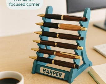 Puede incluir: Un estante para bolígrafos de color turquesa que contiene siete bolígrafos. Los bolígrafos son una mezcla de negro y marrón con detalles dorados. El estante tiene el nombre "HARPER" en la parte delantera. El texto de la imagen dice "Her calm, focused corner" y "Ladder Seven Pen Rack".