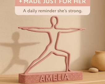 Peut inclure: Une figurine rose représentant une pose de yoga, avec le nom "AMELIA" sur la base. La figurine est dans la pose du guerrier II. Le texte au-dessus de la figurine indique "MADE JUST FOR HER" et "A daily reminder she's strong."