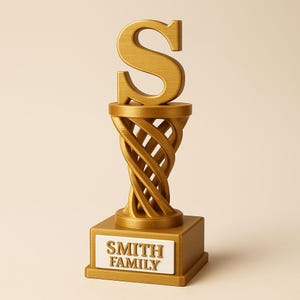 Puede incluir: Un trofeo dorado con la letra "S" en la parte superior. El trofeo tiene un diseño de columna retorcida y una base rectangular con las palabras "SMITH FAMILY" en blanco.