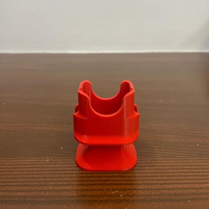 May include: A bright red plastic 3D printed stand with a square base and a U-shaped top.