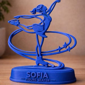 May include: A blue 3D-printed figure skater keepsake. The figure is in a graceful pose, with arms extended and one leg raised. The base reads "SOFIA FIGURE SKATER". The text "A personalized skating keepsake" is above the figure.