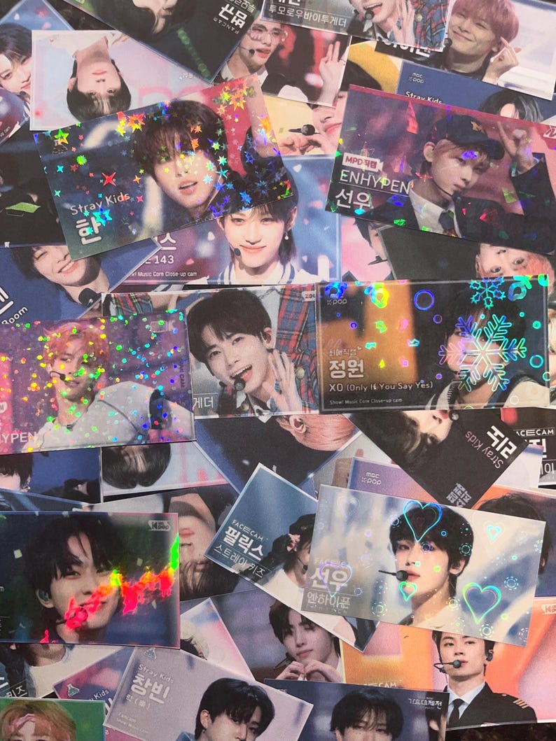 Puede incluir: Una colecci&oacute;n de tarjetas fotogr&aacute;ficas hologr&aacute;ficas de &iacute;dolos del K-pop. Las tarjetas muestran im&aacute;genes de hombres j&oacute;venes con texto en coreano e ingl&eacute;s. Algunas tarjetas presentan los grupos Stray Kids y Enhypen. Las tarjetas tienen un acabado brillante e iridiscente.