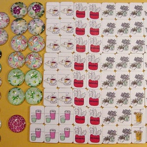 May include: A collection of decorative glass cabochons and square tiles with various designs. The cabochons feature floral, nautical, and abstract patterns. The tiles depict coffee cups, potted plants, and beverages.