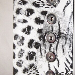 May include: A white and black patterned wallet with a zip closure and silver-coloured hardware. The wallet features a leopard print design with four snap closures.