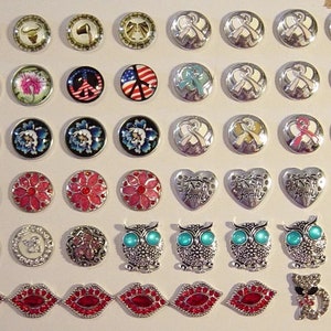 May include: A collection of decorative snap buttons with various designs. The buttons feature floral patterns, butterflies, peace signs, American flags, awareness ribbons, hearts with the word "family", owls with turquoise eyes, lips, and cat designs.