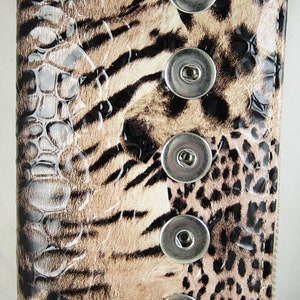 May include: A rectangular wallet with a faux animal print design. The wallet features a combination of leopard and zebra patterns in shades of brown, tan, and black. It has four silver snap closures.