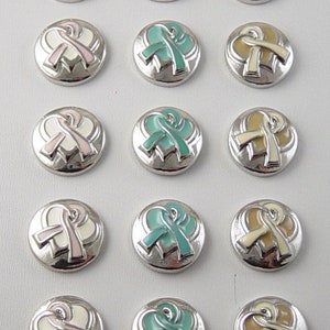 May include: A collection of silver-toned snap buttons with a ribbon design. The ribbons are in various colors, including pink, teal, and yellow, set against a white background. The buttons are round and have a raised design.