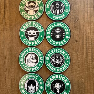Op de afbeelding: Acht ronde groene en zwarte onderzetters met verschillende Disney-personages en de tekst "COFFEE" op elk. De onderzetters tonen personages zoals Stitch, Darth Vader, Baby Yoda, Jack Skellington, Grumpy, Maleficent, Ursula en Simba.