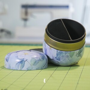 Könnte beinhalten: Eine geteilte, runde, blaue und weiße Blumendose mit goldfarbenem Rand und schwarzem Innenraum. Die Dose ist geöffnet und der Deckel liegt daneben.