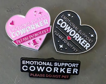 Puede incluir: Tres pines de esmalte con el texto "EMOTIONAL SUPPORT COWORKER" y "PLEASE DO NOT PET". Dos pines tienen forma de corazón, uno rosa y otro negro, mientras que el tercero es un pin rectangular negro con letras blancas y rojas.