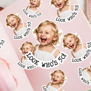 May include: A collection of die-cut stickers featuring a smiling blonde child in a white dress. Each sticker includes the black text "LOOK WHO'S 50!" arranged in a circular arc below the child's portrait, showcasing a joyful expression.