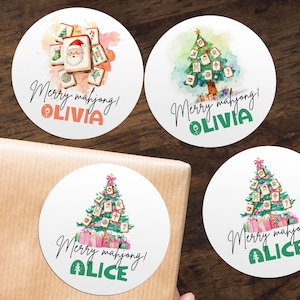 May include: Four white round stickers with watercolor illustrations and text. Two stickers feature a Christmas tree decorated with Mahjong tiles, and two feature Mahjong tiles with a Santa. The text reads "Merry mahjong!" and a name.