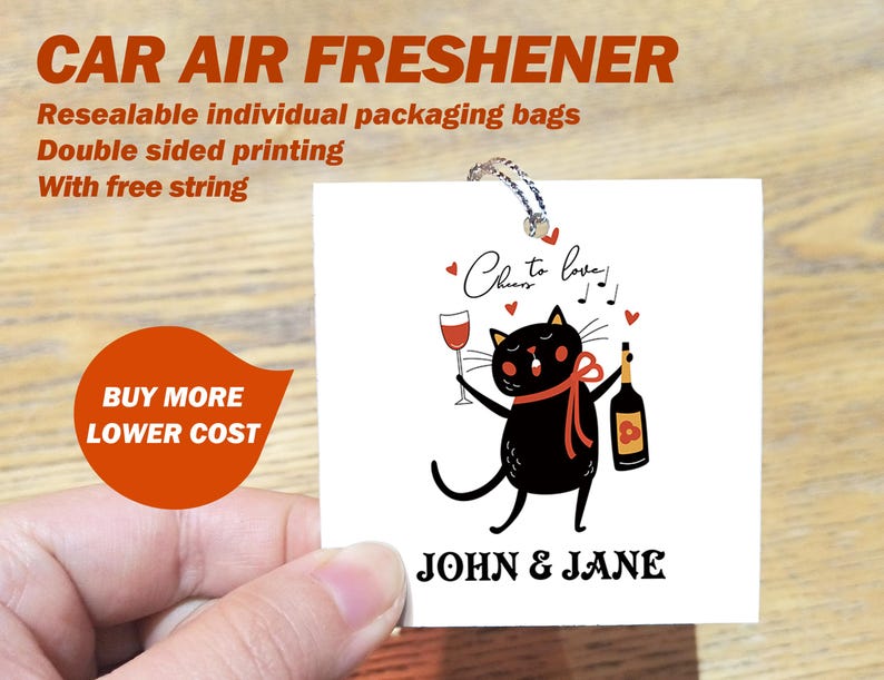 Op de afbeelding: Een witte autoluchtverfrisser met een illustratie van een zwarte kat die een glas wijn en een fles wijn vasthoudt. De tekst "Cheers to love!" en "John & Jane" staat op de luchtverfrisser gedrukt.