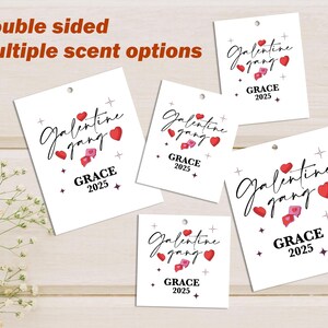 May include: Several white tags with the words "Galentine gang" in a script font, red hearts, and "GRACE 2025". The tags have a small hole at the top and are displayed on a light wood surface. The text "Double sided" and "Multiple scent options" are also visible.
