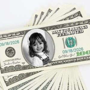 Puede incluir: Un abanico de billetes personalizados de 100 d&oacute;lares con un retrato en blanco y negro de una ni&ntilde;a. Los billetes presentan el texto "MAY YOU ALWAYS FEEL LOVED" y "God Bless You!" con la fecha 09/18/2026 y el nombre "Sandra's Baptism".