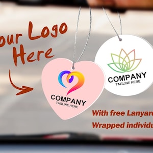 May include: Two air fresheners hanging by strings. One is heart-shaped, light pink, with a colorful logo and the text "COMPANY TAGLINE HERE." The other is round, white, with a green and pink floral logo and the text "COMPANY TAGLINE HERE."