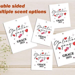 May include: Several white tags with the words "Galentine gang" in a script font, red hearts, and "GRACE 2025". The tags have a small hole at the top and are displayed on a light wood surface. The text "Double sided" and "Multiple scent options" are also visible.