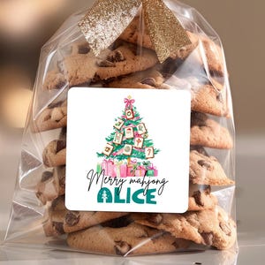 May include: A clear cellophane bag filled with chocolate chip cookies, tied with a gold ribbon. A square label features a Christmas tree decorated with mahjong tiles, gifts, and the text "Merry mahjong ALICE".
