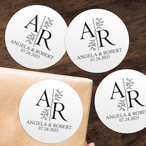 Peut inclure: Trois autocollants ronds blancs avec des motifs floraux noirs et le texte "A R Angela & Robert 07.24.2025".