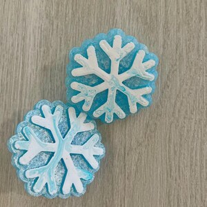 May include: Two blue snowflake-shaped ornaments with white snowflake designs. The snowflakes have a marbled effect.
