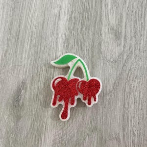 May include: A red and green glitter cherry charm with a dripping effect.