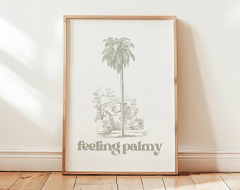 May include: A framed art print featuring a detailed sketch of a palm tree and other foliage in a light green hue. The phrase "feeling palmy" is printed in a matching green font below the illustration. The artwork is displayed in a natural wood frame.